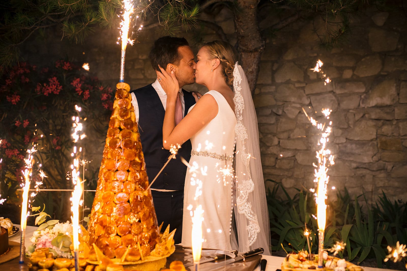 bride and groom kiss in front of cake and sparklers
