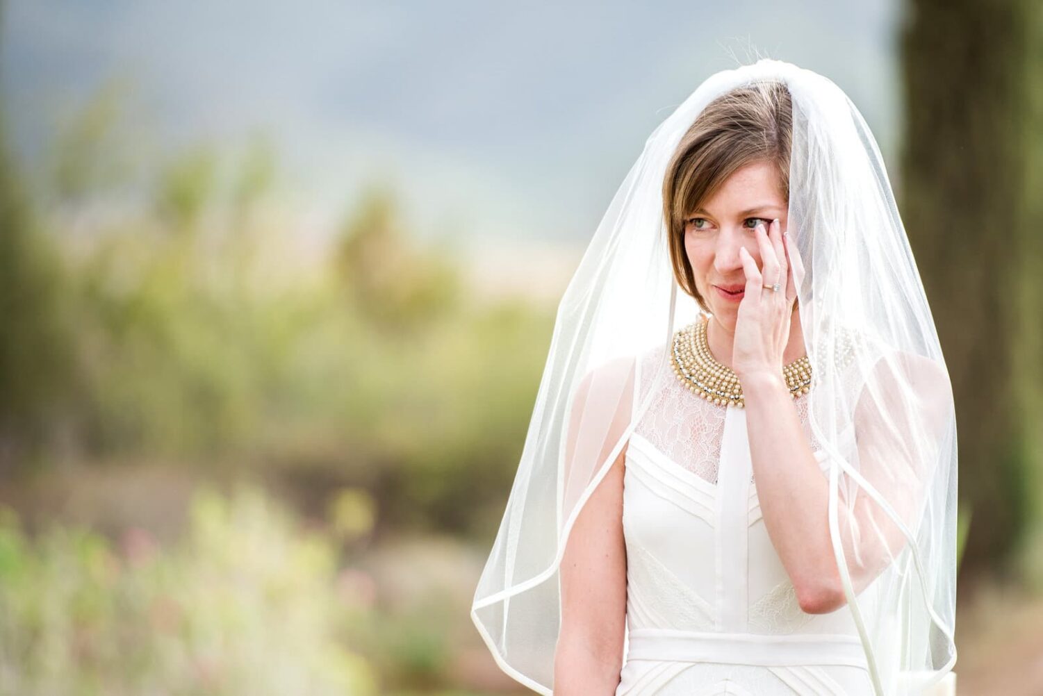 bride wiping tear away during outdoor ceremony