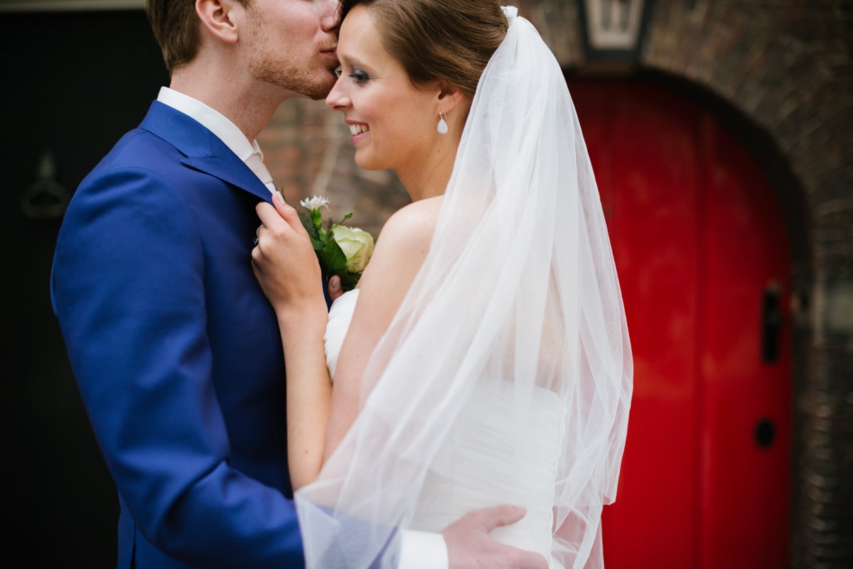 bride and groom kissing in front of red door