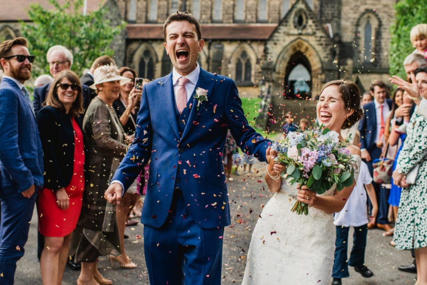 couple laughing walking through confetti outside church