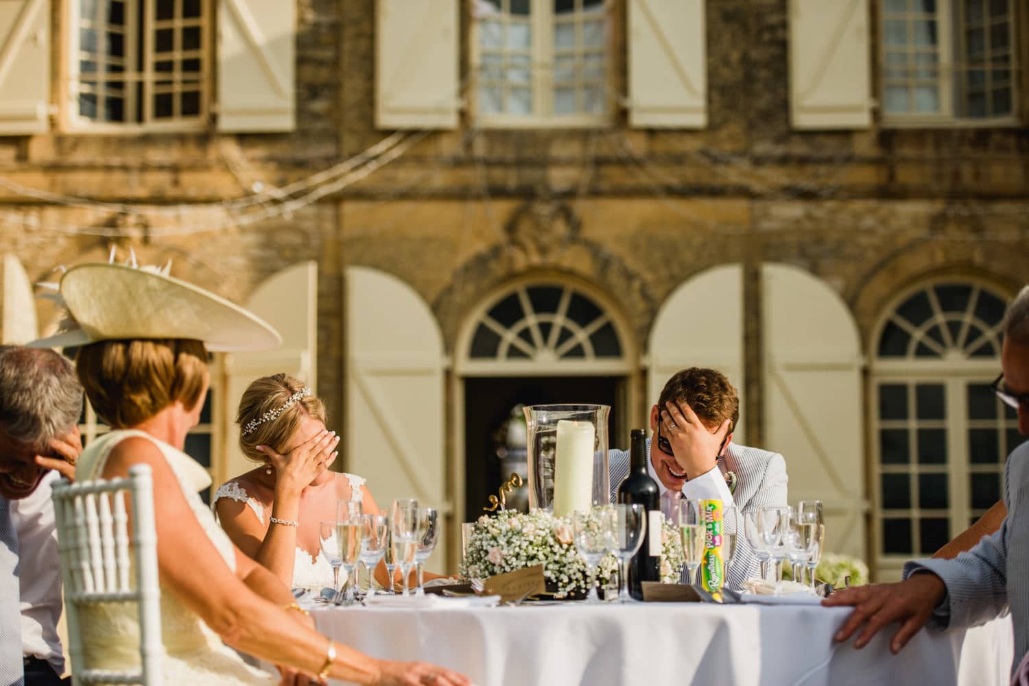 bride and groom with hands cover their faces during the speeches